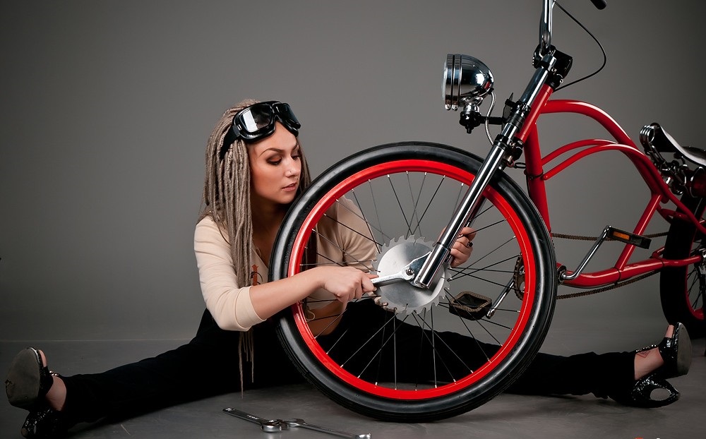 Девушка чинит красный велосипед