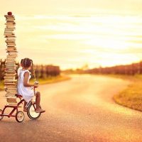 Девочка на велосипеде с горой книг при закате