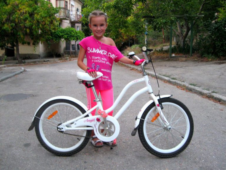 Девочка восьми лет в розовом рядом с белым велосипедом