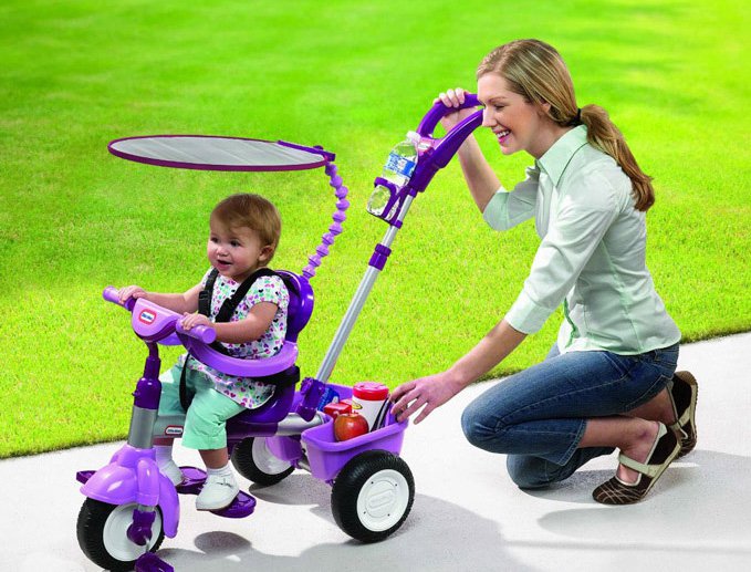 Девушка и ребенок на трехколесном фиолетовом велосипеде с ручкой