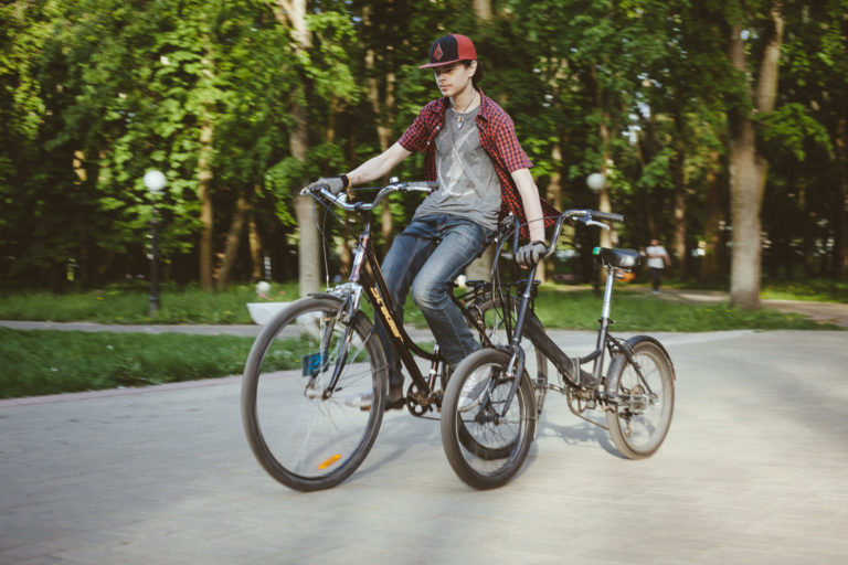 Подросток на велосипеде придерживает рядом велосипед