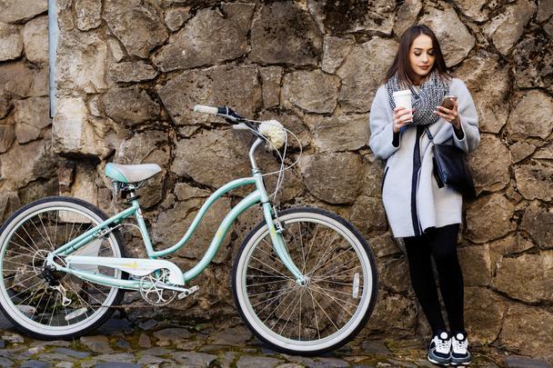 Девушка с городским велосипедом на фоне каменной стены
